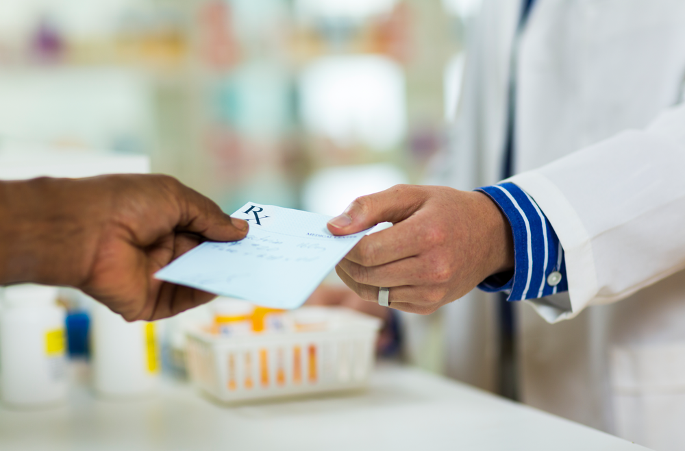 A pharmacist handing a prescription over a counter to a patient